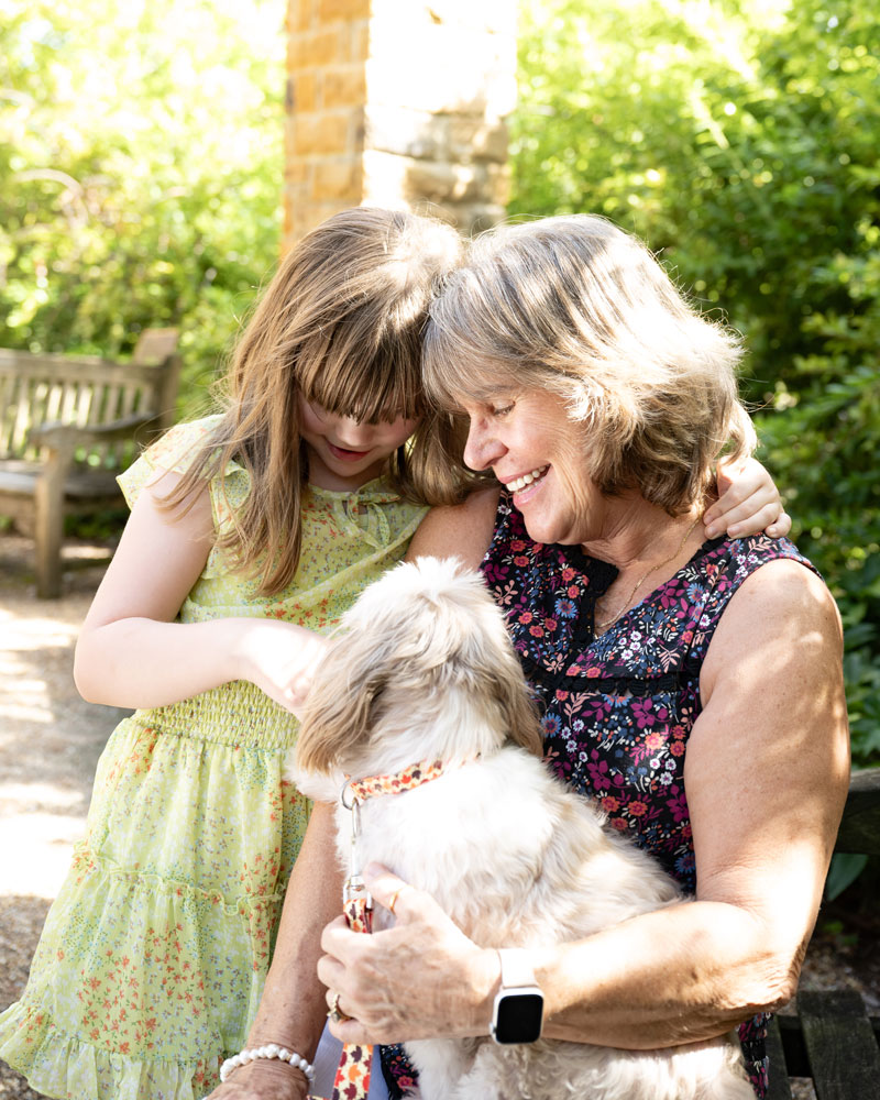 A grandmother and granddaughter playing with their dog in a park.